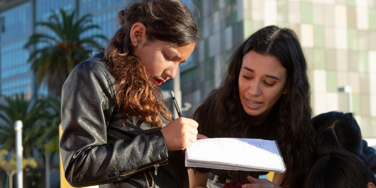 Adult and student write in a notepad outdoors.