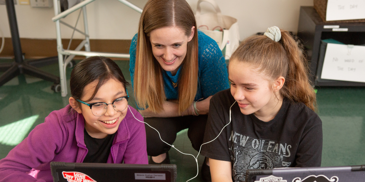 Woman working with two students as they look at a laptop.